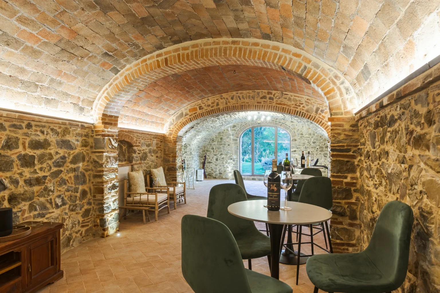Cozy wine tasting room featuring arched brick ceilings and stone walls, with modern furniture and a view of the garden through large windows. | Only on SopranoVillas