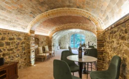 Cozy wine tasting room featuring arched brick ceilings and stone walls, with modern furniture and a view of the garden through large windows.