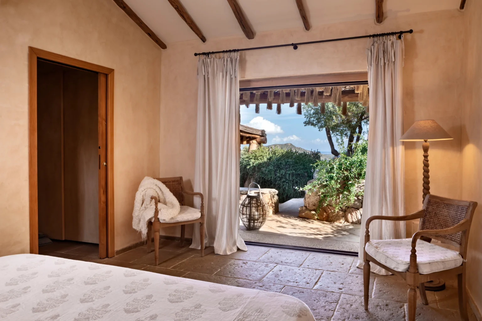 Luxurious bedroom in a villa for rent in Italy, featuring elegant decor, natural light streaming through large curtains, and a picturesque view of the garden outside. | Only on SopranoVillas