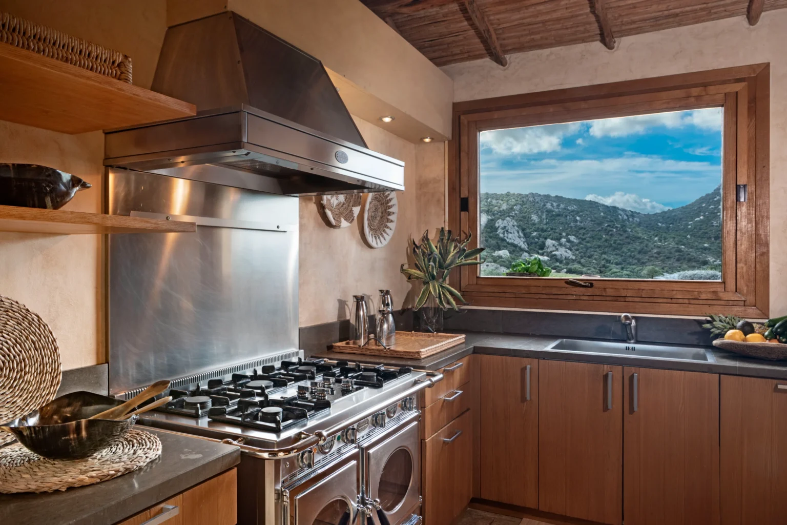 Luxury villa kitchen in Italy featuring modern appliances, wooden cabinetry, and scenic mountain views through a large window, perfect for an upscale vacation experience. | Only on SopranoVillas