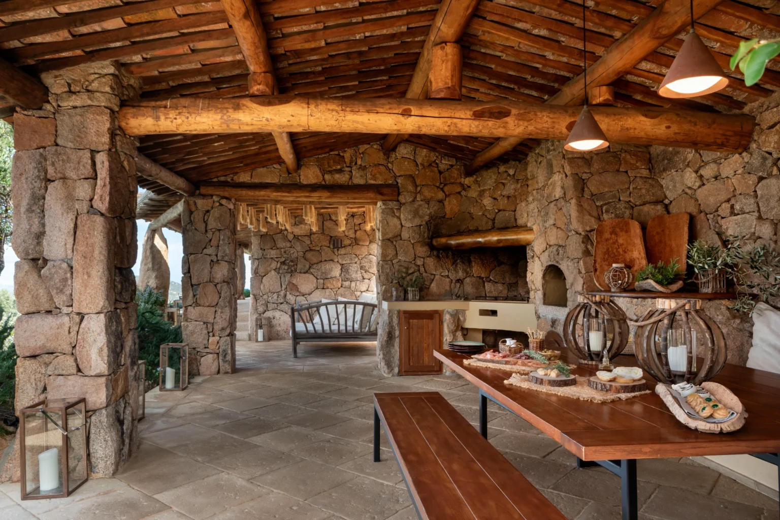 Luxury villa rental in Italy featuring a rustic stone outdoor dining area with wooden beams, a spacious table, and elegant decor, perfect for relaxing and entertaining. | Only on SopranoVillas