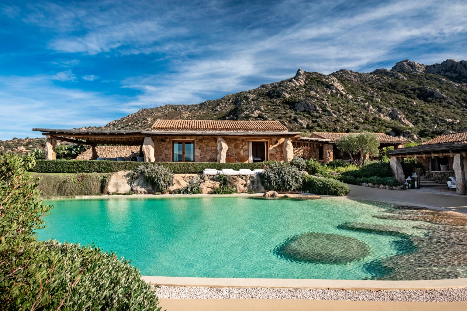 Luxury villa for rent in Italy featuring a stunning outdoor pool surrounded by lush greenery and mountains, ideal for a relaxing getaway. | Only on SopranoVillas