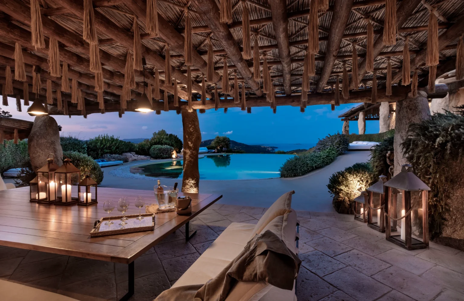 Luxury villa rental in Italy featuring an elegant outdoor lounge area with ambient lighting, stunning views of the pool and landscape, perfect for relaxation and entertaining at sunset. | Only on SopranoVillas