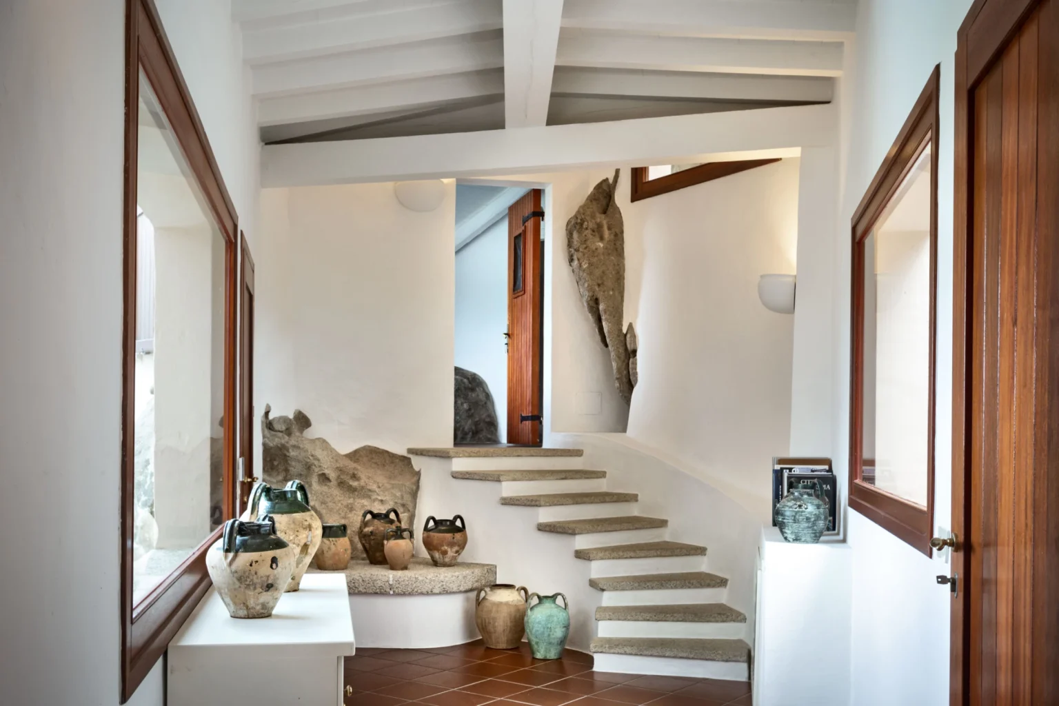 Modern interior hallway featuring a staircase, natural light, and decorative pottery. The white walls and wooden accents create a warm and inviting atmosphere. | Only on SopranoVillas