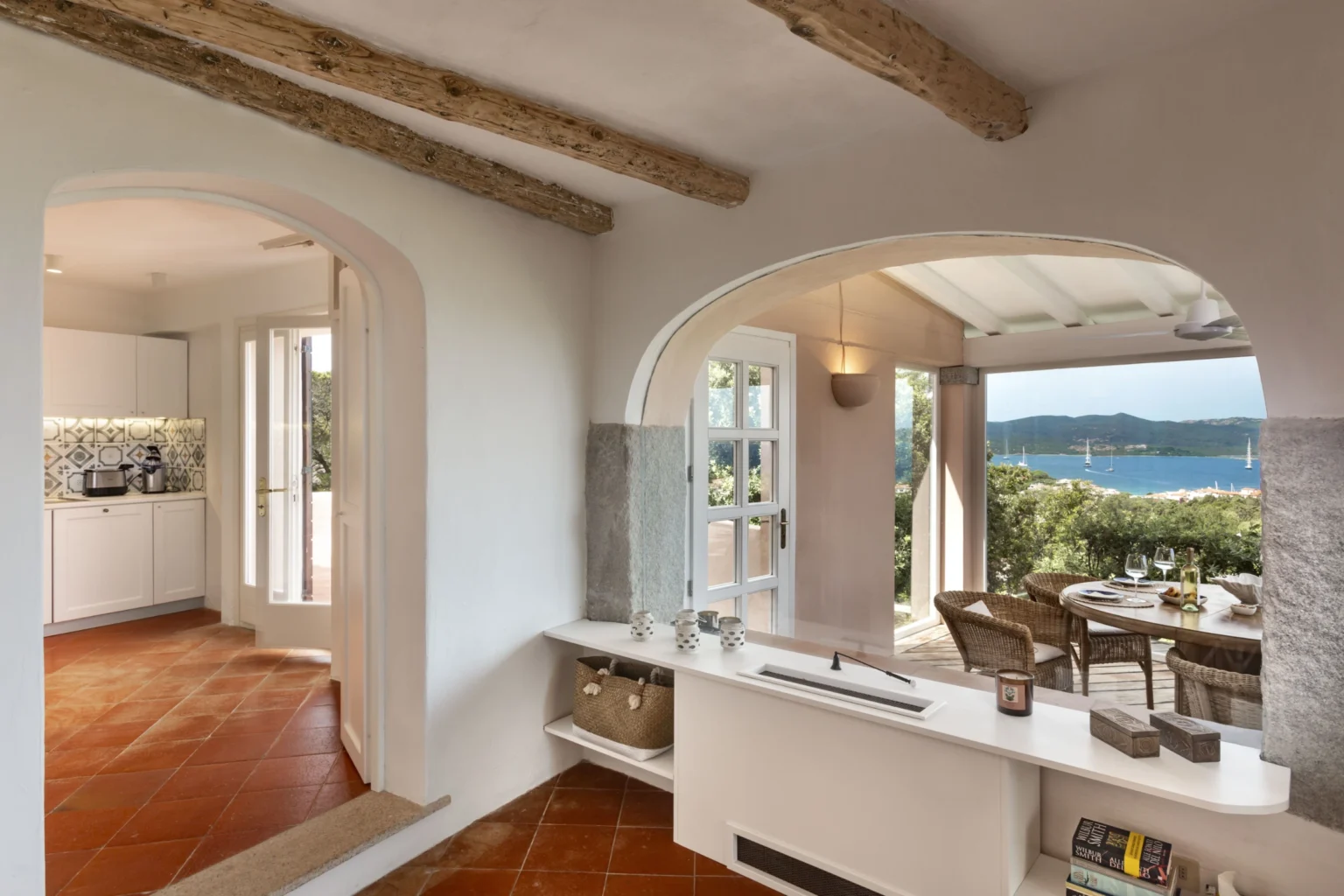 Spacious interior of a coastal home featuring rustic wooden beams, an open layout, and large windows offering a scenic view of the ocean. The design blends modern and traditional elements, creating a warm and inviting atmosphere. | Only on SopranoVillas