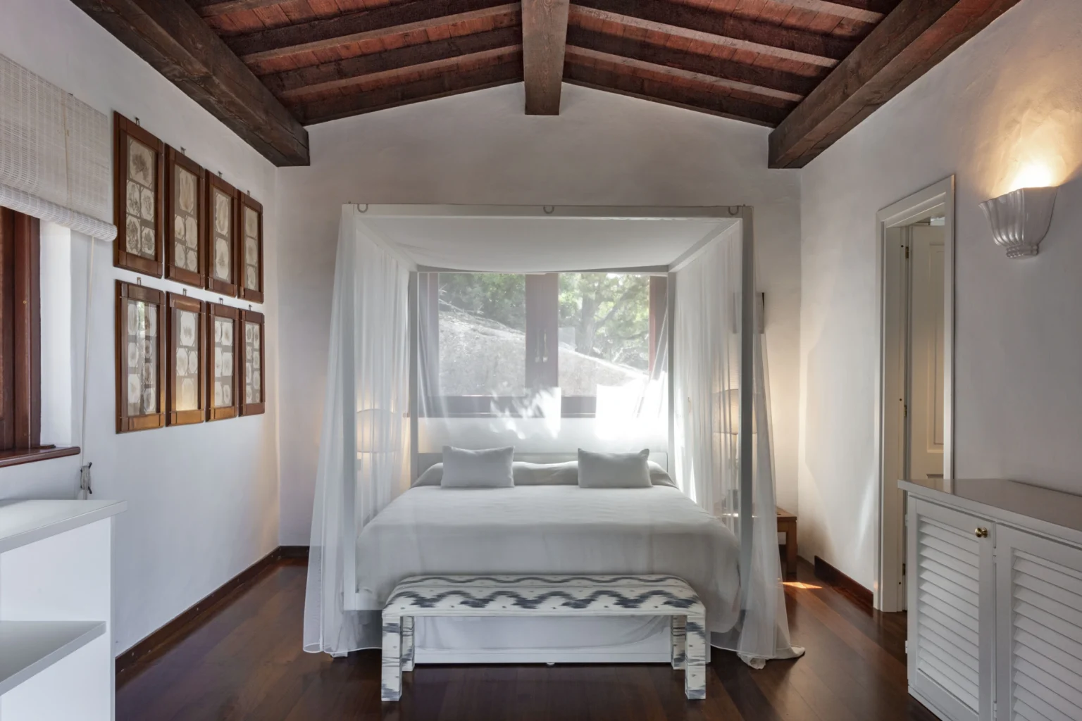 Modern bedroom with a canopy bed, natural light streaming through large windows, and wooden beams on the ceiling, creating a serene and inviting atmosphere. | Only on SopranoVillas