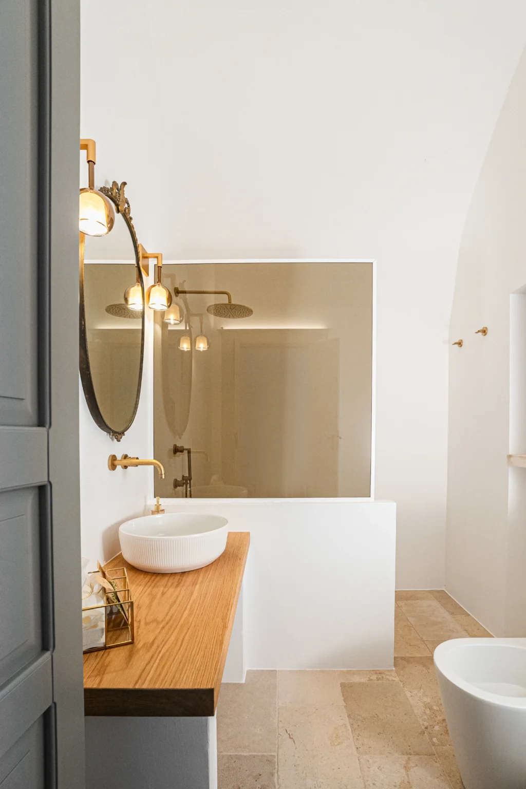 Modern bathroom interior featuring a round mirror, elegant gold fixtures, and a minimalist white sink on a wooden countertop. Soft lighting creates a warm ambiance. | Only on SopranoVillas