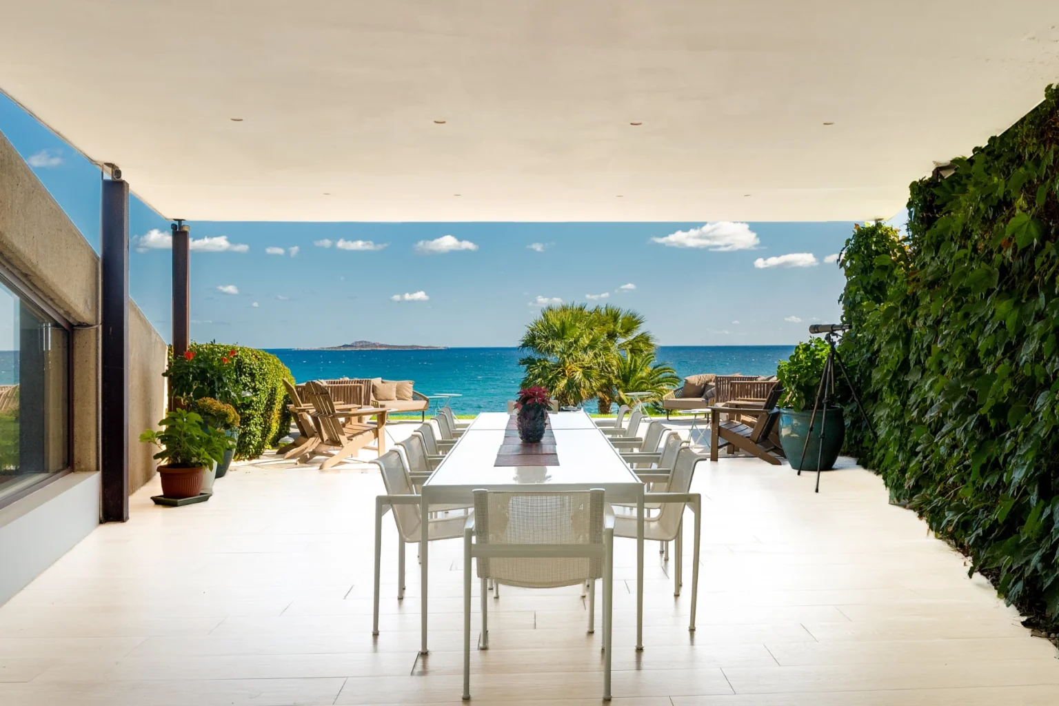 Modern outdoor dining area with a large table and chairs, featuring a stunning ocean view and lush greenery, perfect for entertaining and enjoying nature. | Only on SopranoVillas