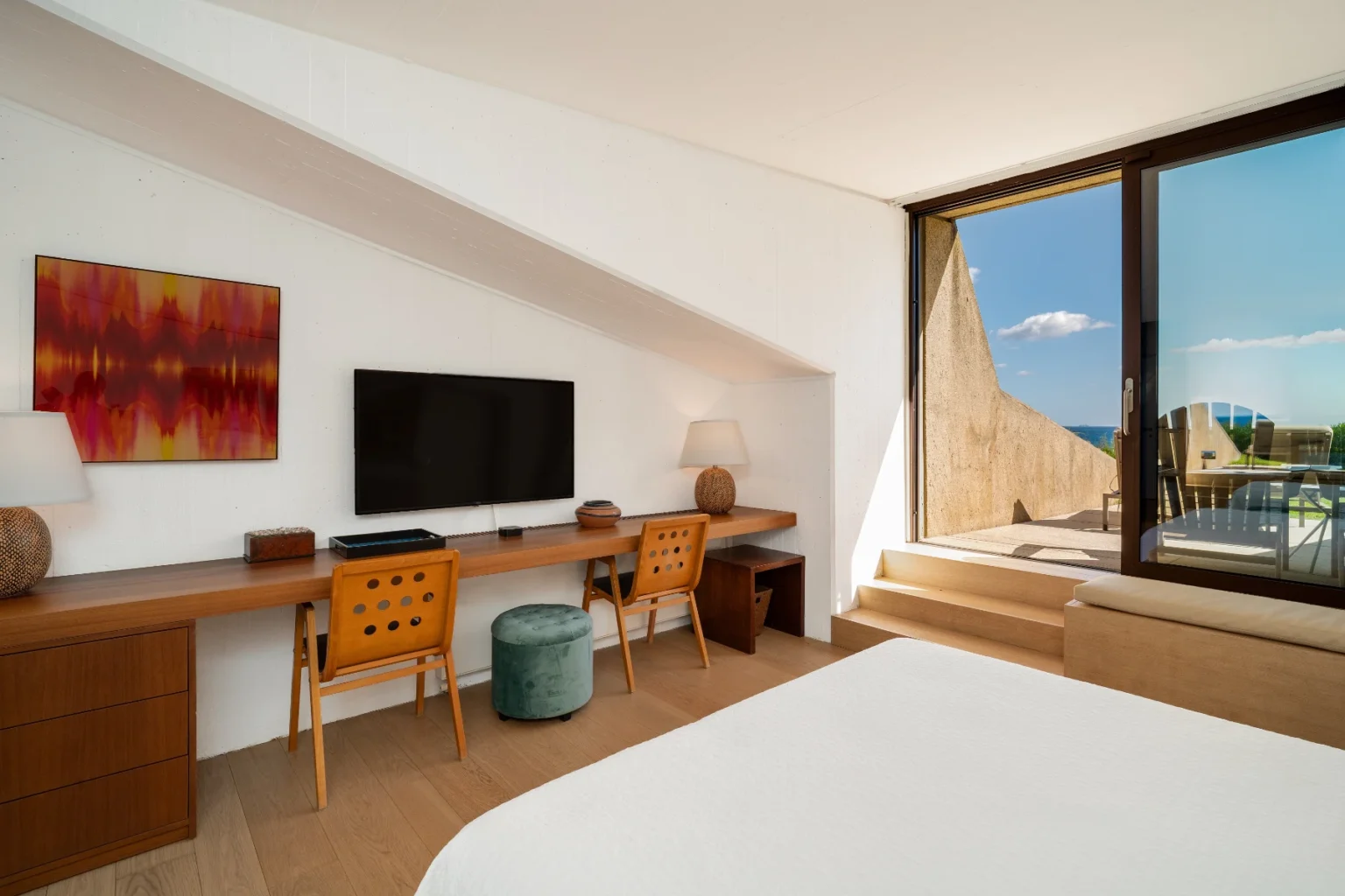 Modern hotel room featuring a spacious layout, a large window with scenic views, a wooden desk with stylish chairs, a flat-screen TV, and contemporary decor. | Only on SopranoVillas