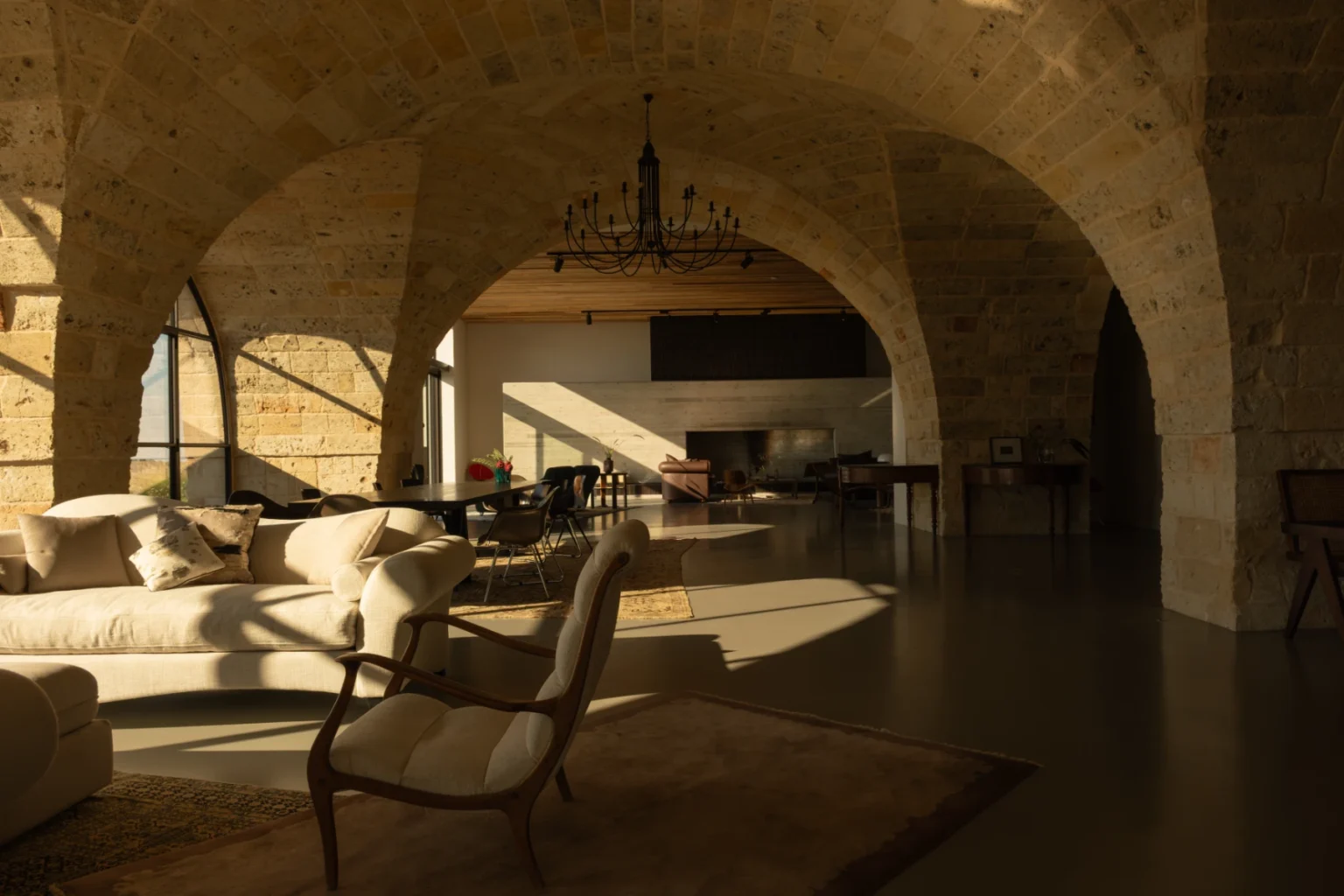 Spacious living room with stone arches, elegant chandelier, and modern furnishings, showcasing natural light and a cozy atmosphere. | Only on SopranoVillas