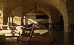 Spacious living room with stone arches, elegant chandelier, and modern furnishings, showcasing natural light and a cozy atmosphere.
