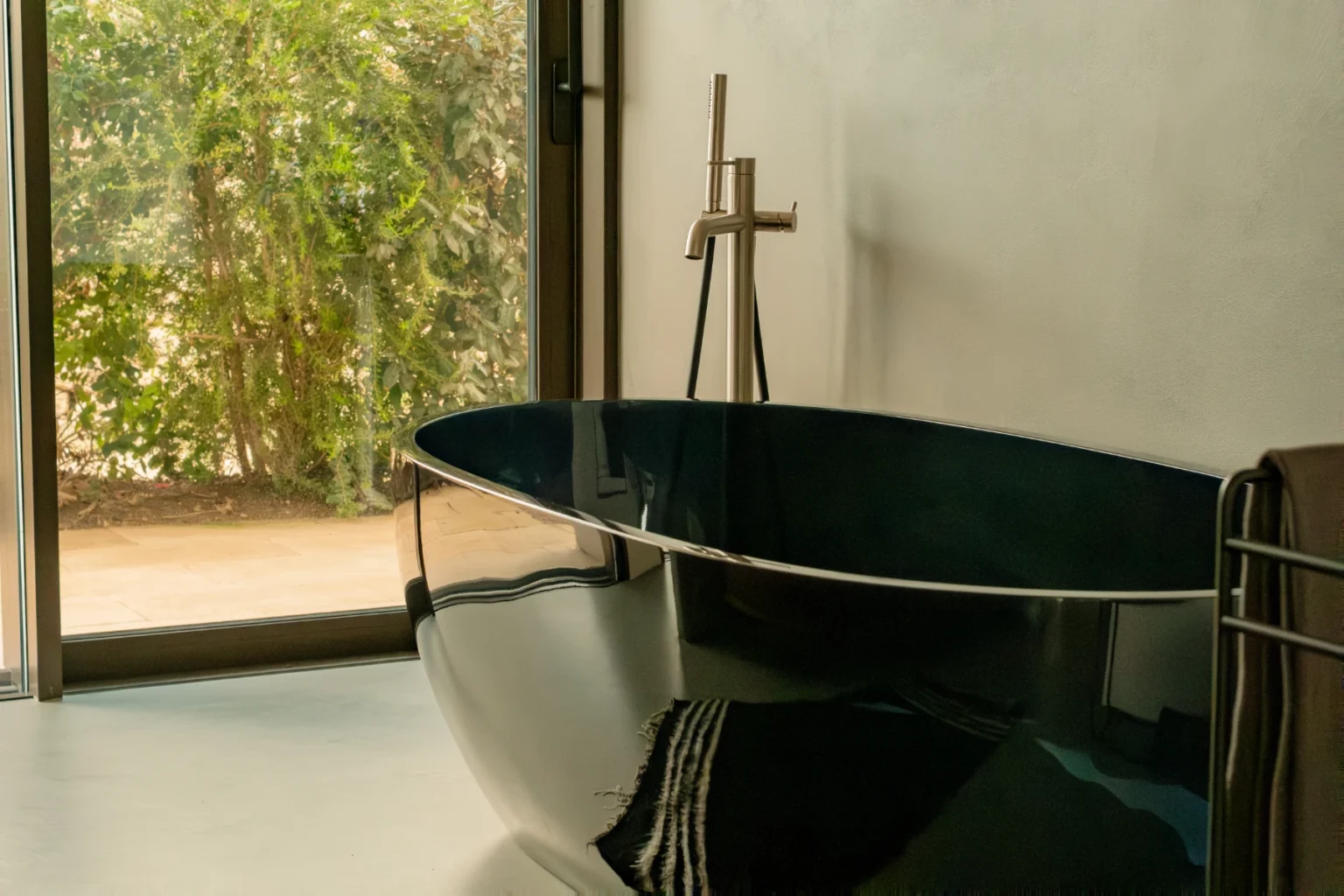 Modern bathroom featuring a sleek, black freestanding bathtub, complemented by natural light streaming through large windows and a minimalistic decor. | Only on SopranoVillas