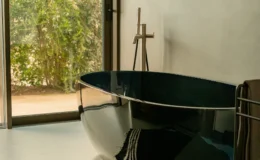 Modern bathroom featuring a sleek, black freestanding bathtub, complemented by natural light streaming through large windows and a minimalistic decor.