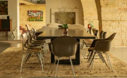 Modern dining room featuring a large black table surrounded by stylish brown chairs, set on a decorative rug. The space is illuminated with natural light and decorated with flowers and artwork, creating an inviting atmosphere for gatherings.