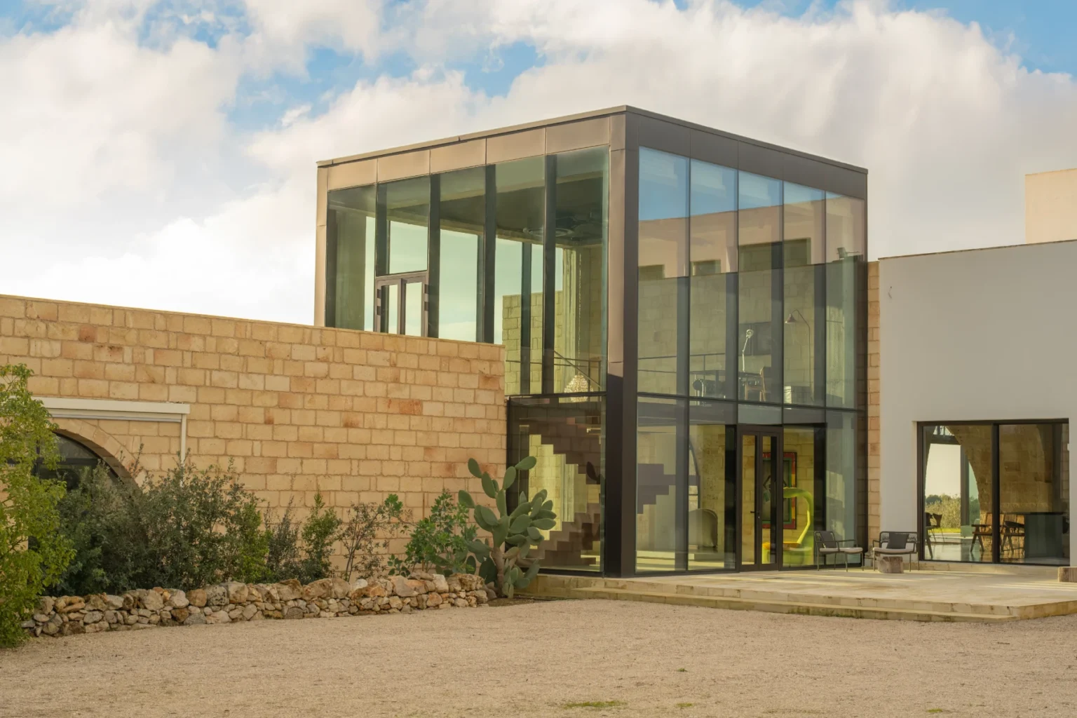Modern architectural design featuring a glass and stone house with a spacious outdoor area, surrounded by greenery under a cloudy sky. | Only on SopranoVillas