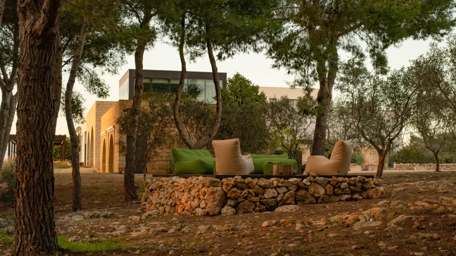 Cozy outdoor seating area surrounded by trees and stone walls, featuring green cushions and a natural setting. Modern house in the background adds a contemporary touch to the serene landscape. | Only on SopranoVillas