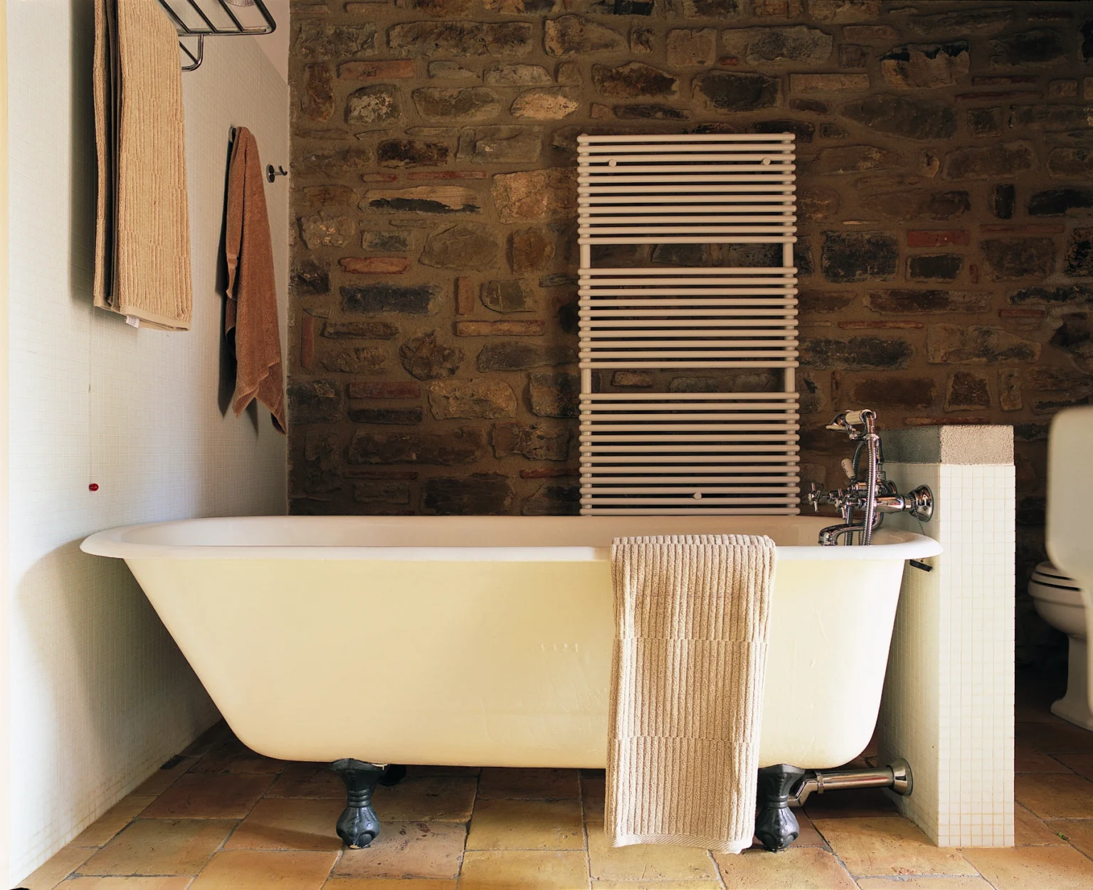 Cozy bathroom featuring a vintage freestanding bathtub, stone wall accents, a towel rack, and neutral-colored towels, creating a warm and inviting atmosphere. | Only on SopranoVillas