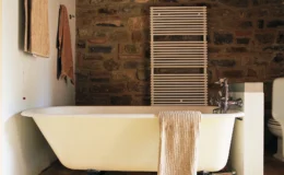Cozy bathroom featuring a vintage freestanding bathtub, stone wall accents, a towel rack, and neutral-colored towels, creating a warm and inviting atmosphere.