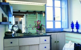 Bright and modern kitchen interior featuring light green striped walls, a sleek dark countertop, and decorative blue glass vases. Natural light floods through a large window, enhancing the vibrant atmosphere.