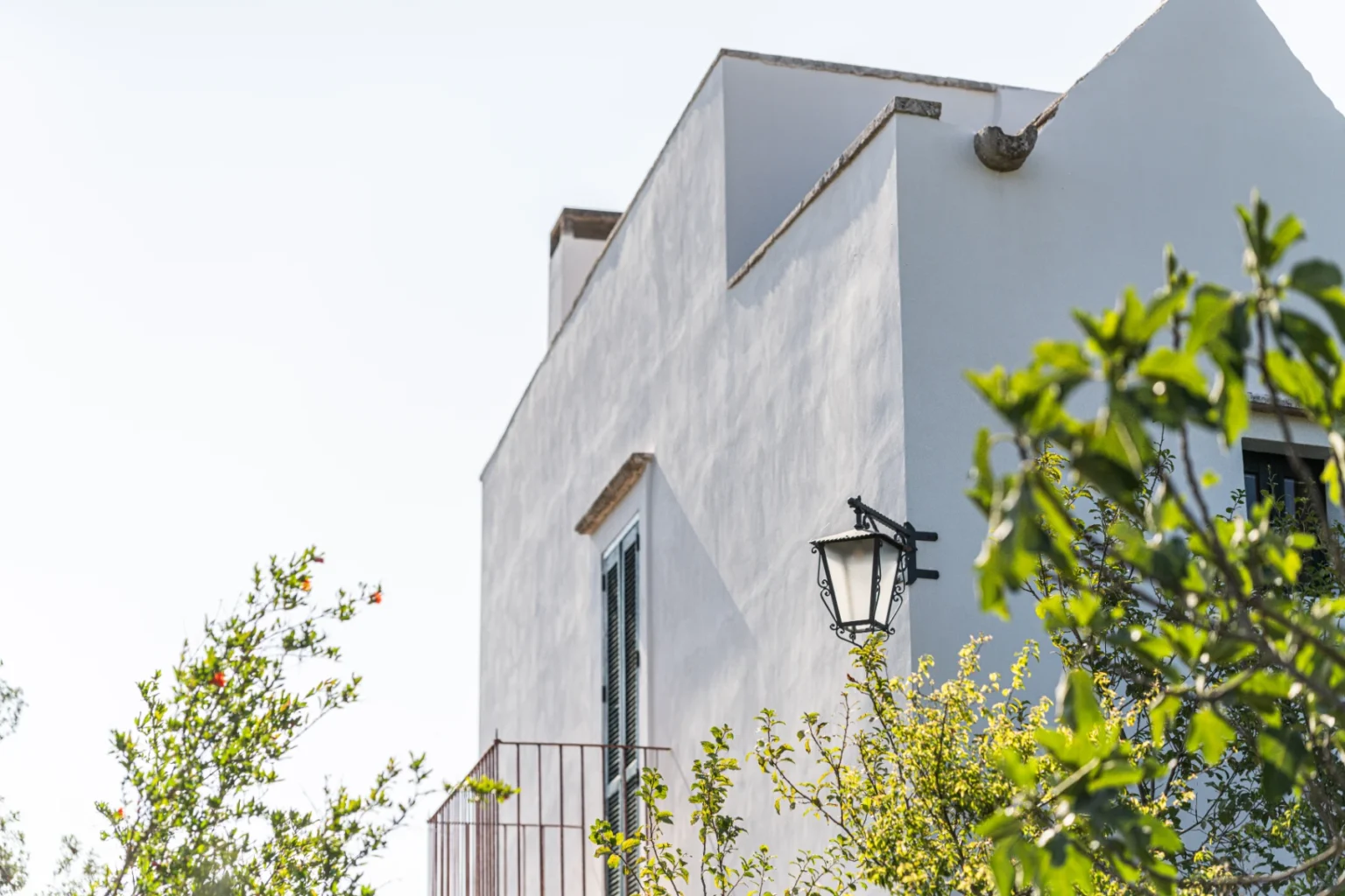 White modern house with a balcony and a vintage lamp, surrounded by greenery under a clear sky. | Only on SopranoVillas