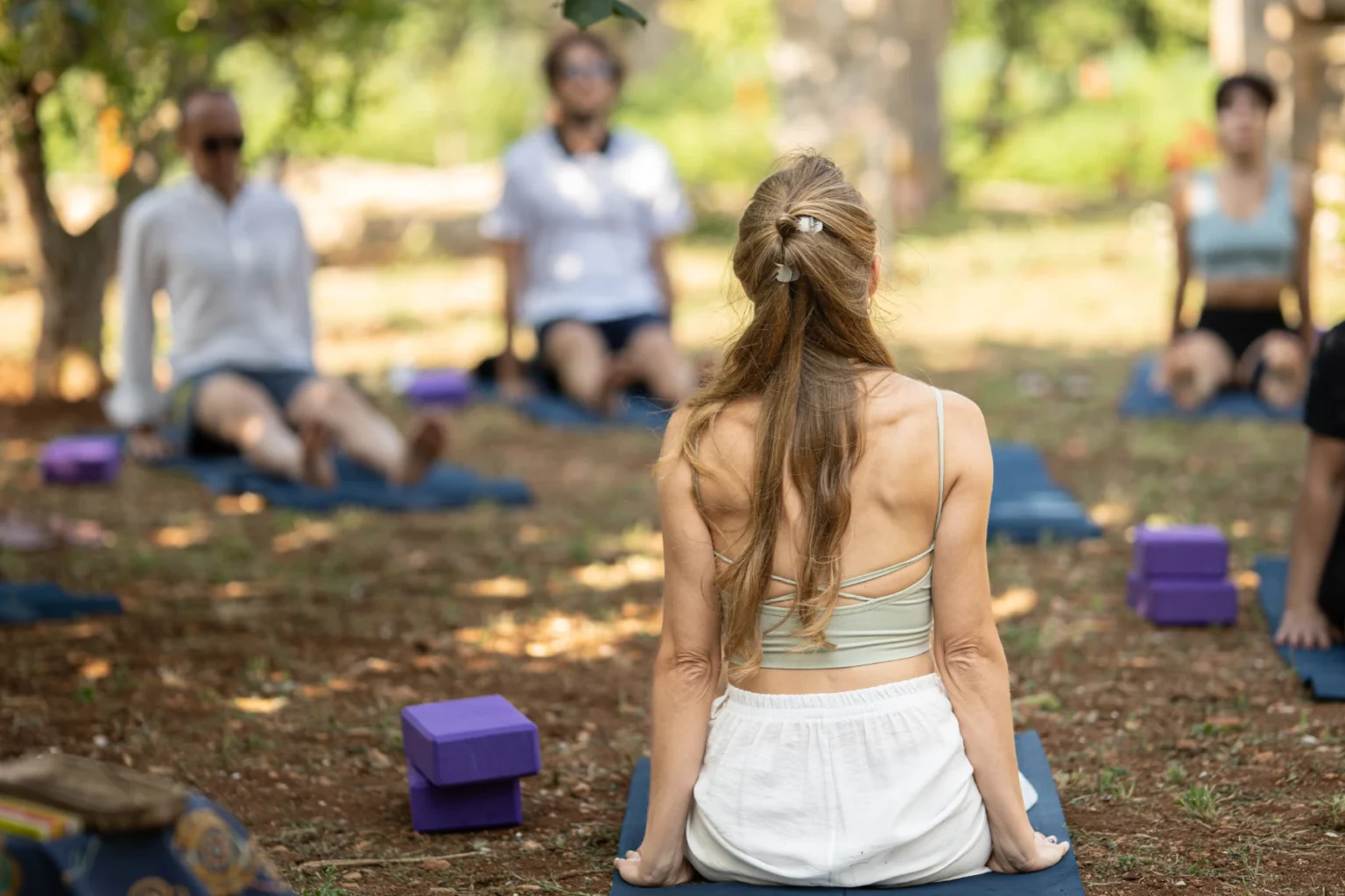 Outdoor yoga class with participants practicing mindfulness and meditation on mats surrounded by nature, featuring a woman in a light outfit leading the session. | Only on SopranoVillas