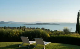 Scenic view of a tranquil lake surrounded by lush greenery, featuring two lounge chairs on a grassy area, perfect for relaxation and enjoying the serene landscape.