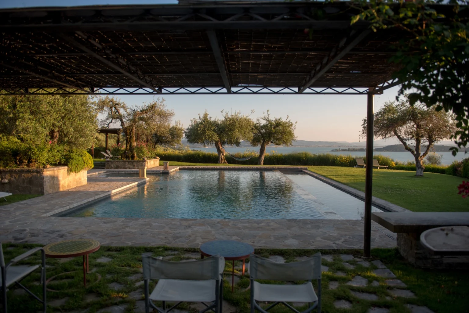 Scenic view of a modern outdoor pool surrounded by olive trees, with a spacious lawn and patio furniture. Ideal for relaxation and outdoor gatherings. | Only on SopranoVillas