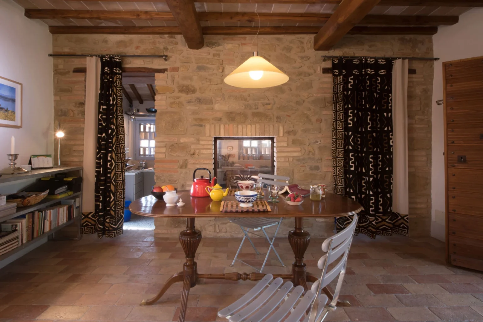 Cozy dining area featuring a wooden table set with colorful dishes, surrounded by rustic stone walls and warm wooden beams. Natural light illuminates the space, enhancing the inviting atmosphere. | Only on SopranoVillas