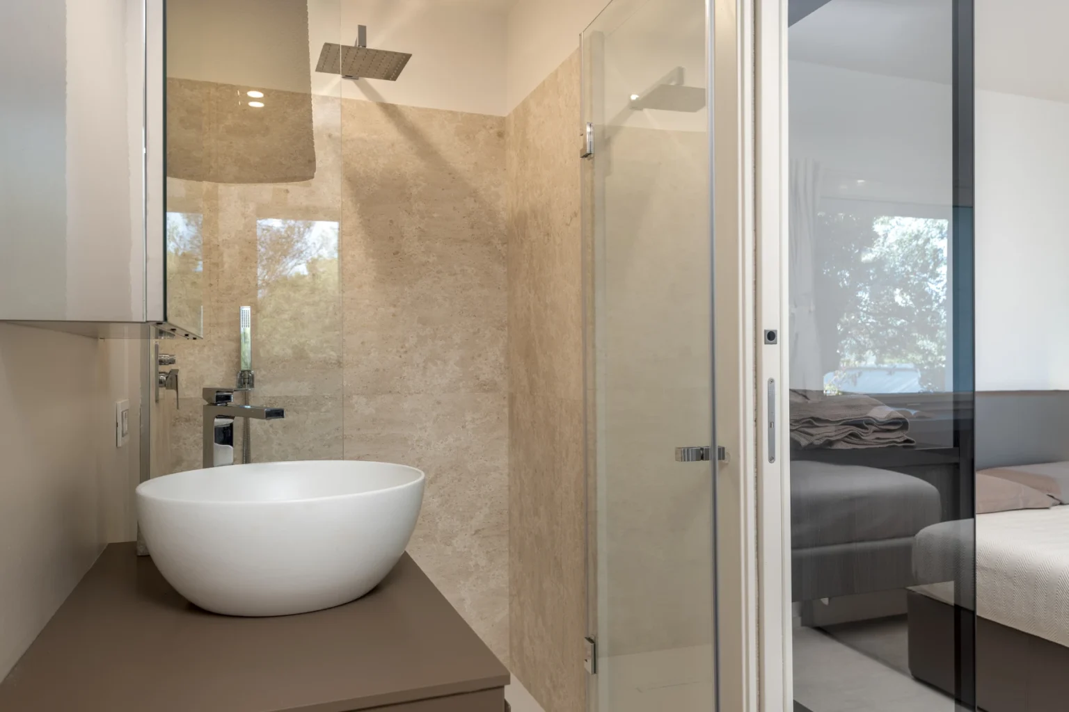 Modern bathroom featuring a stylish freestanding white sink, a glass shower enclosure, and neutral-toned wall tiles, creating a sleek and contemporary aesthetic. | Only on SopranoVillas
