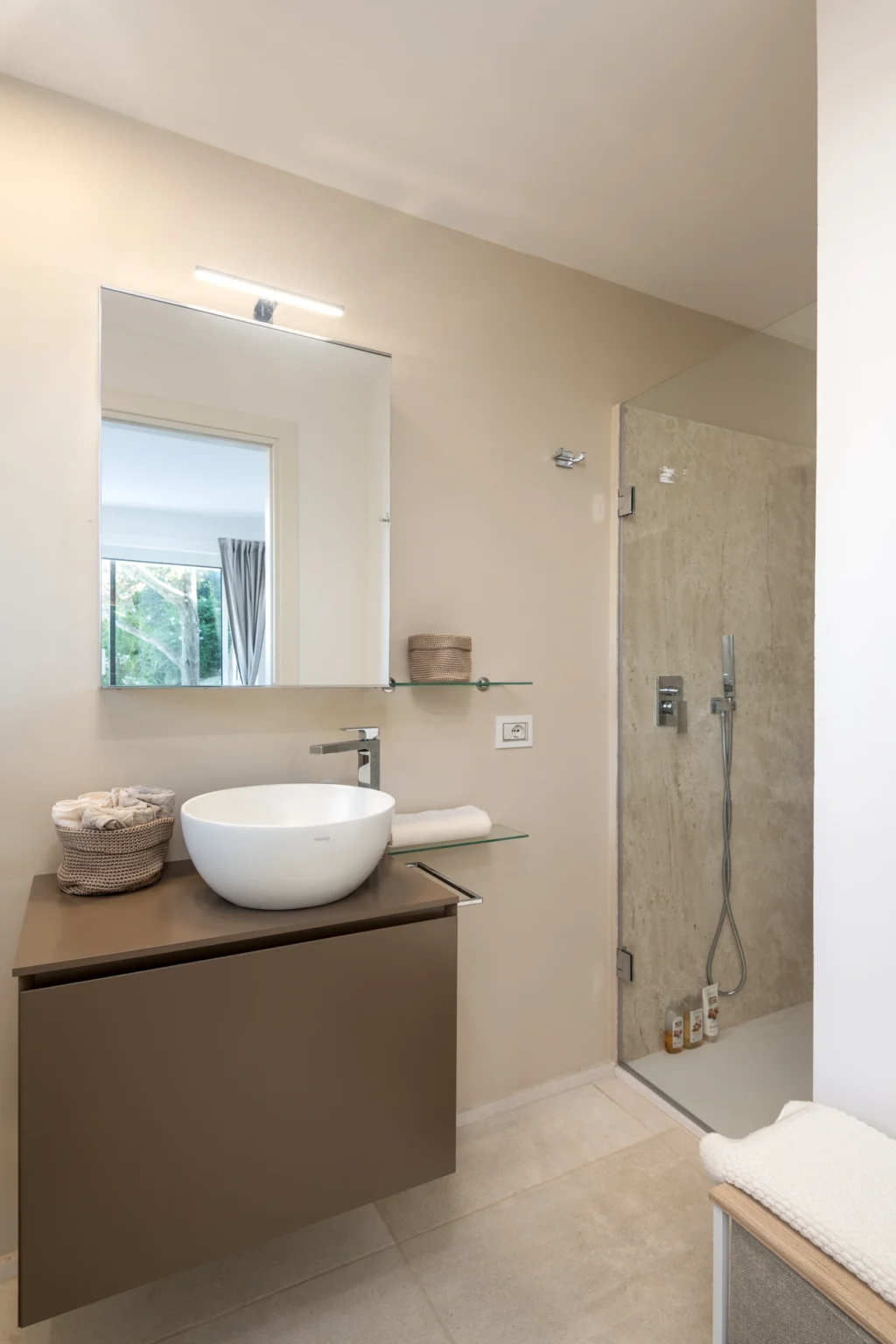 Modern bathroom interior featuring a stylish vessel sink on a wooden countertop, a large mirror, and a glass shower enclosure. Natural light floods the space, highlighting neutral tones and minimalist decor. | Only on SopranoVillas