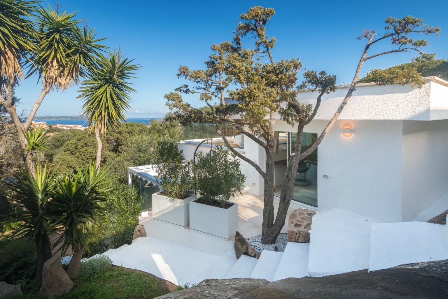 Modern coastal home with white architecture surrounded by greenery and palm trees, featuring a scenic view of the ocean. | Only on SopranoVillas