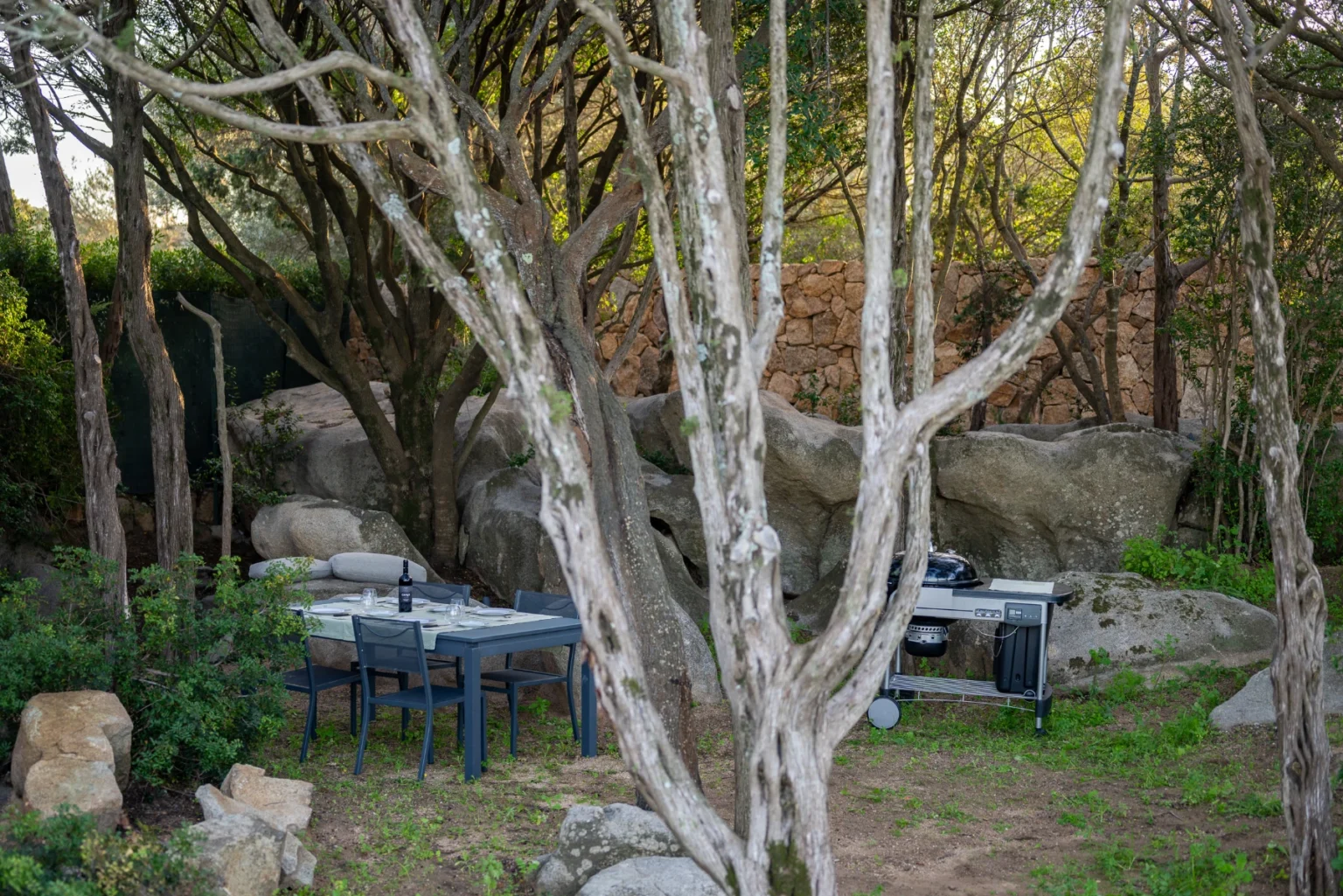 Outdoor dining area surrounded by trees and rocks, featuring a table and chairs, ideal for relaxation and nature gatherings. | Only on SopranoVillas