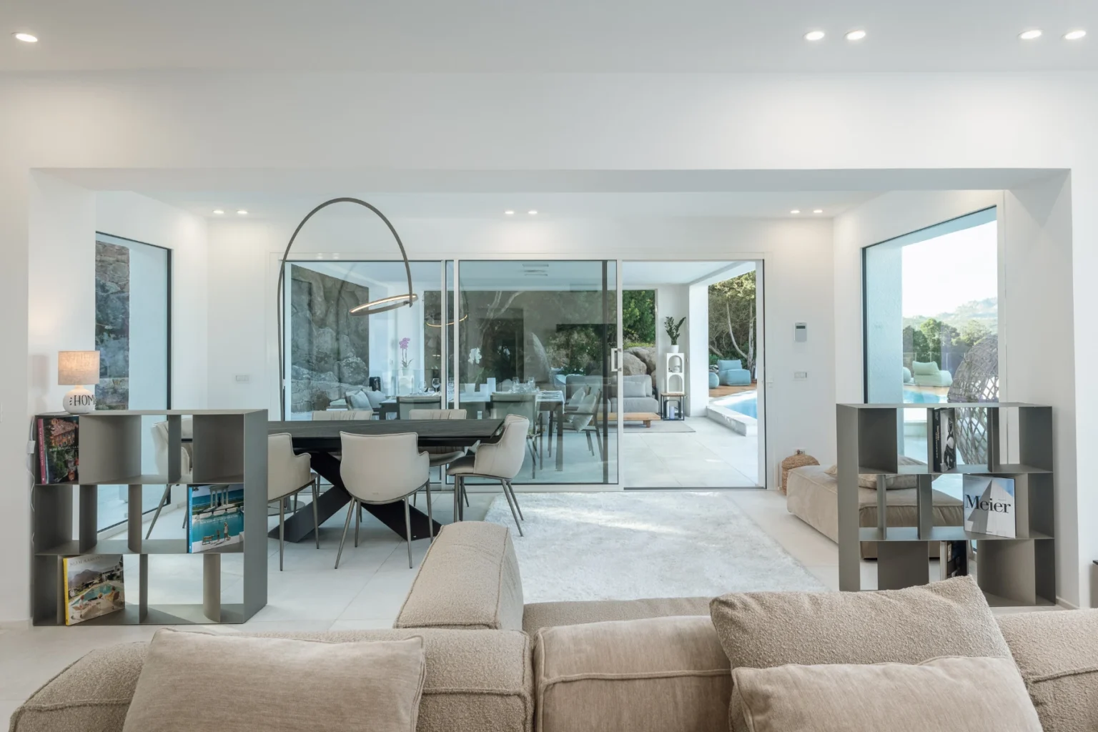 Modern living room featuring a neutral color palette, large windows, and an open layout. The space includes a comfortable beige sofa, a stylish dining area, and views of an outdoor pool. Ideal for contemporary home design inspiration. | Only on SopranoVillas