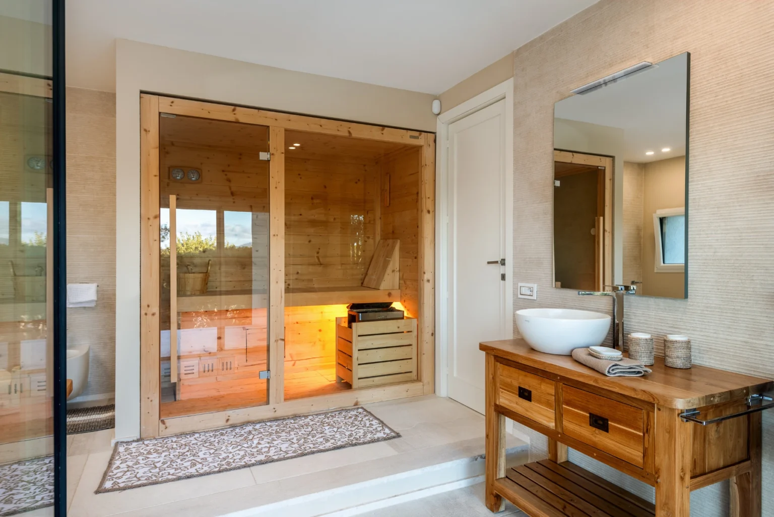 Modern bathroom featuring a wooden sauna, sleek sink, and a stylish mirror, complemented by a decorative rug and contemporary decor. | Only on SopranoVillas