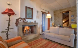 Cozy living room featuring a stone fireplace, a comfortable beige sofa, and warm lighting. The decor includes a colorful area rug and a unique floor lamp, creating an inviting atmosphere.