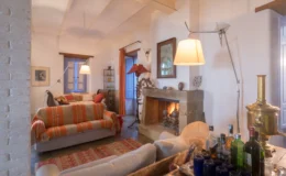Cozy living room featuring a comfortable sofa with colorful throw pillows, a stone fireplace, and warm lighting. The decor includes artwork on the walls and a bar cart with various bottles, creating an inviting atmosphere.