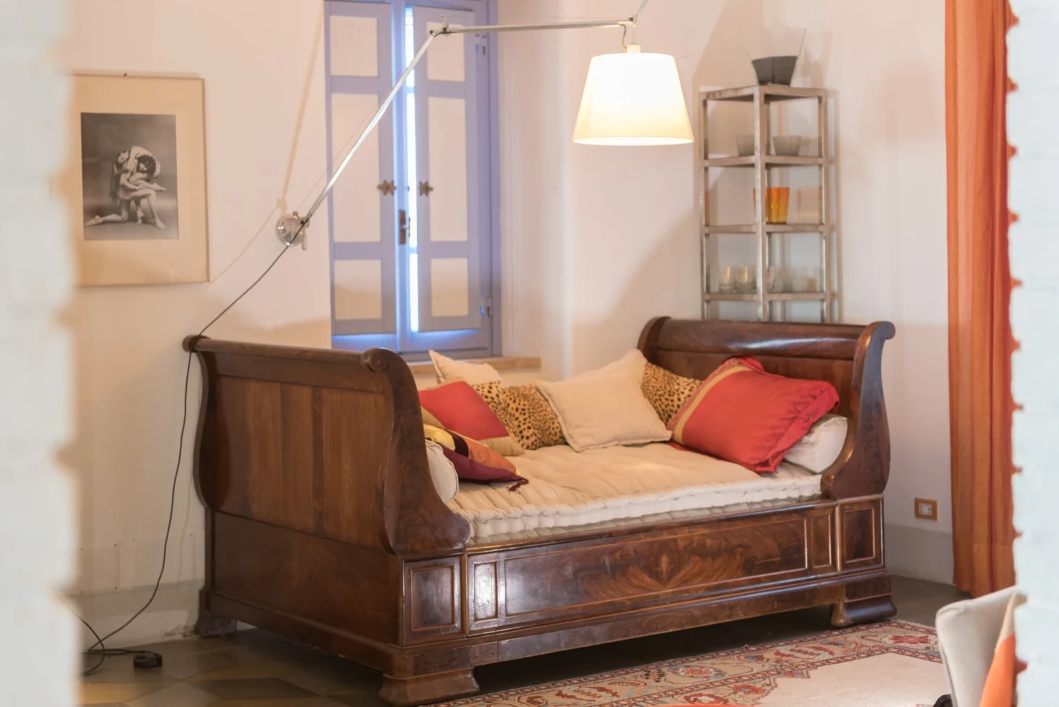 Cozy living room featuring a vintage wooden daybed adorned with colorful cushions, a modern pendant lamp, and a charming window with blue shutters, creating a warm and inviting atmosphere. | Only on SopranoVillas