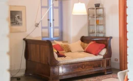 Cozy living room featuring a vintage wooden daybed adorned with colorful cushions, a modern pendant lamp, and a charming window with blue shutters, creating a warm and inviting atmosphere.