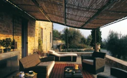 Cozy outdoor patio with wicker furniture and a shaded area, surrounded by greenery and stone walls, ideal for relaxation and entertaining.
