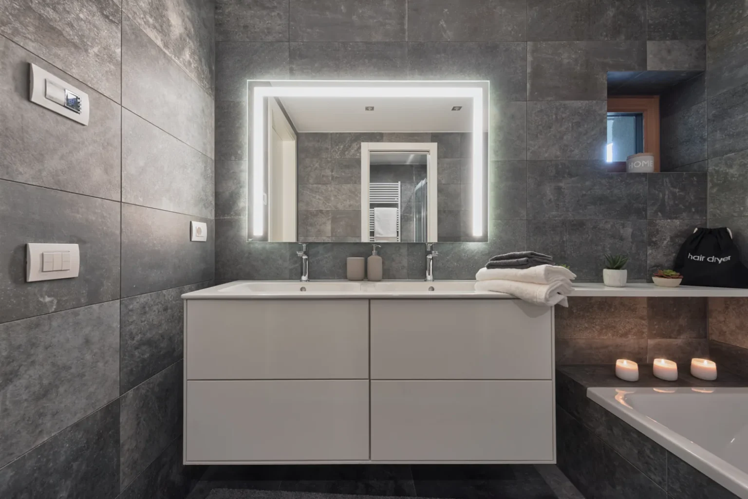 Bathroom with a wide white vanity, an illuminated mirror and a bathtub with candles. | Only on SopranoVillas