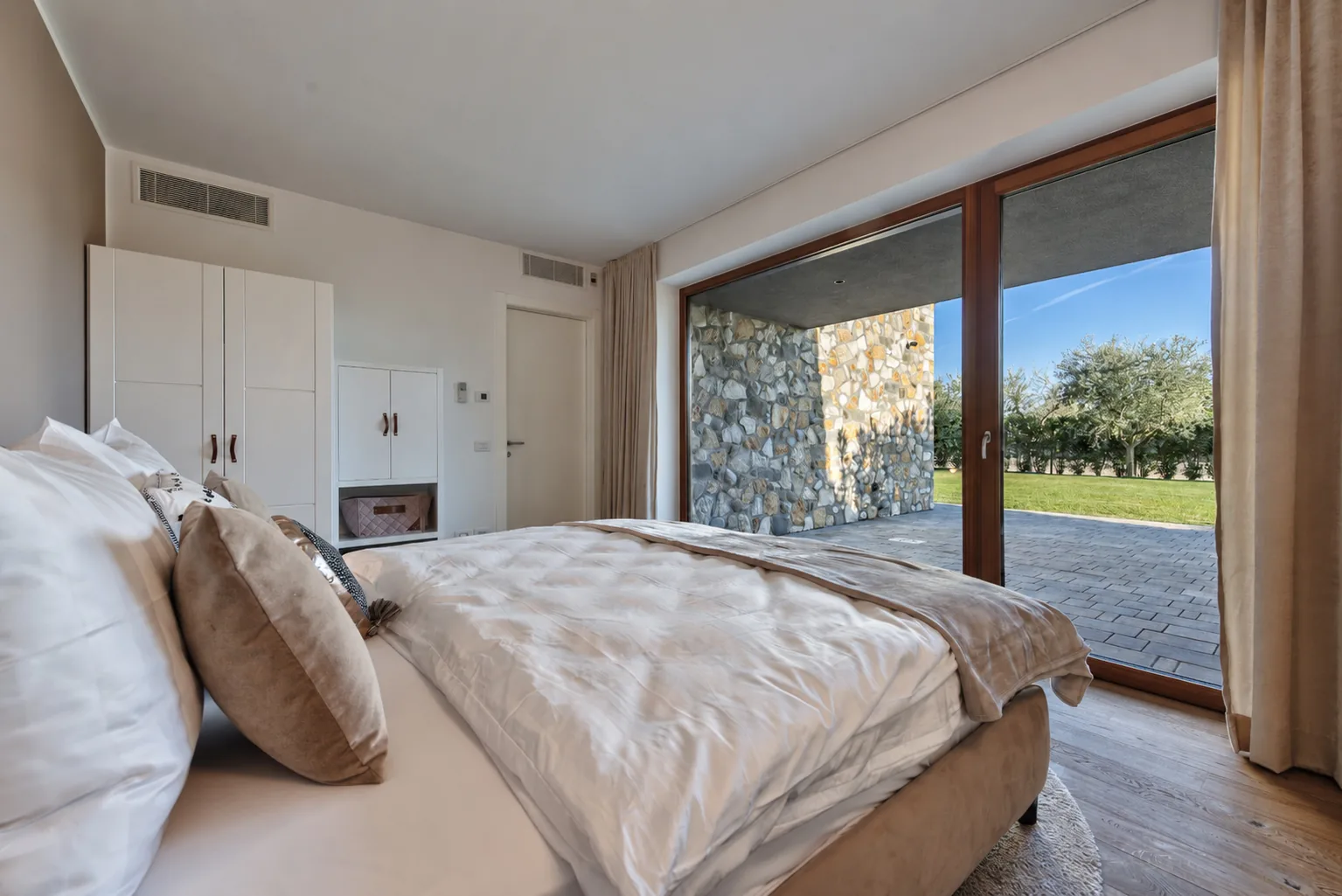 View from the bed through glass doors to a covered stone patio and lawn. | Only on SopranoVillas