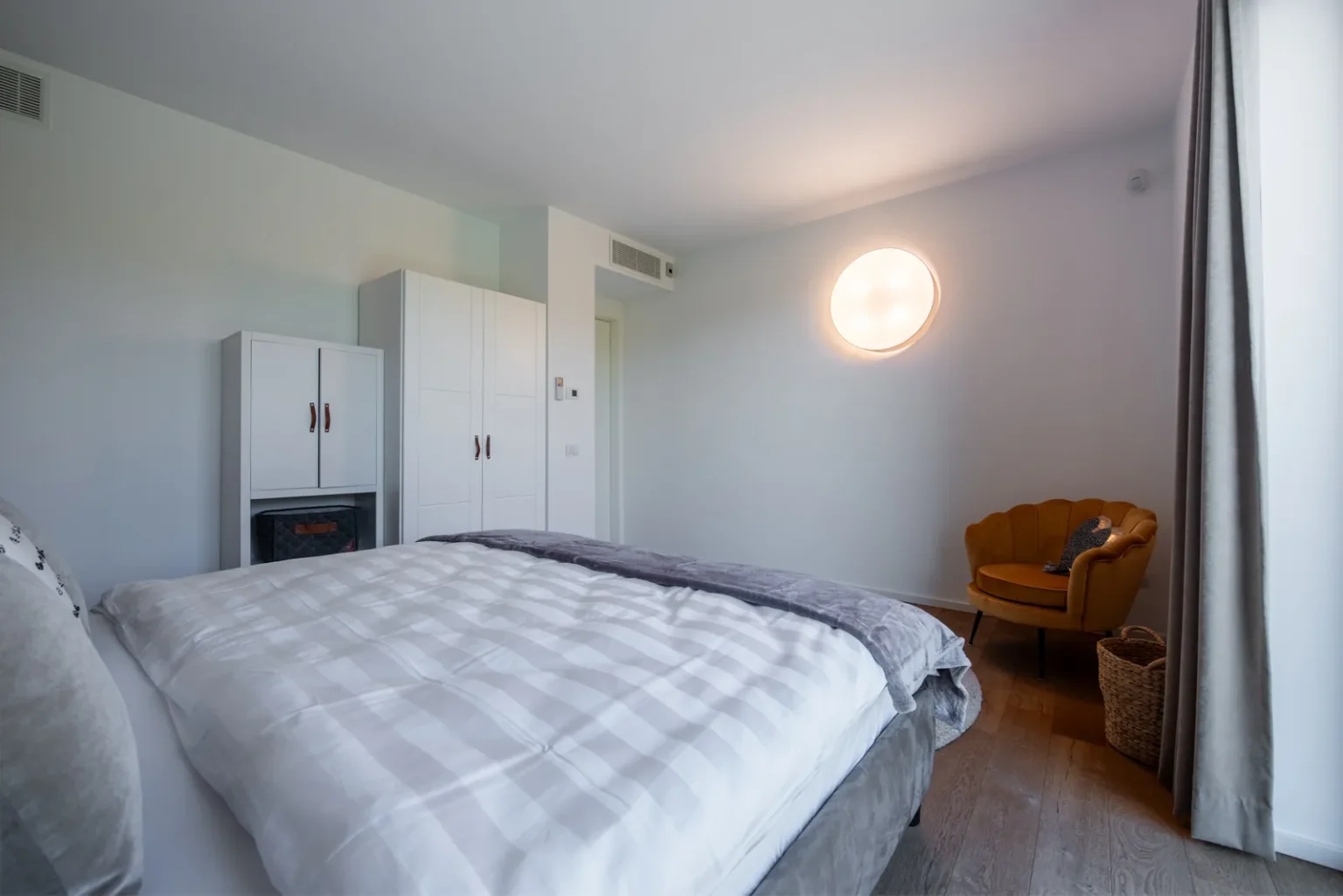 Bedroom with white wardrobes, a round wall light and a yellow armchair beside the bed. | Only on SopranoVillas