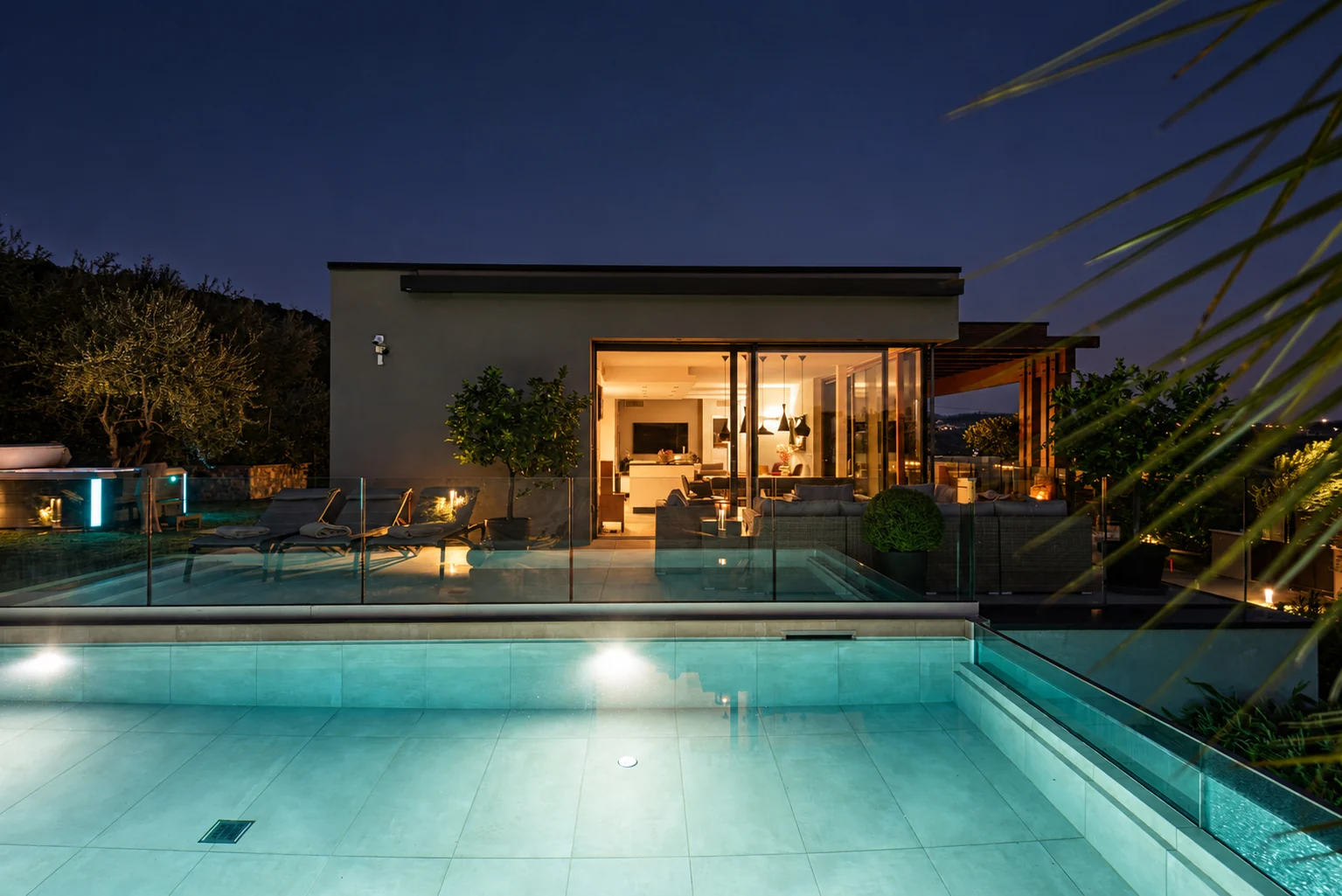Illuminated swimming pool at night facing the villa's glass-fronted living area. | Only on SopranoVillas