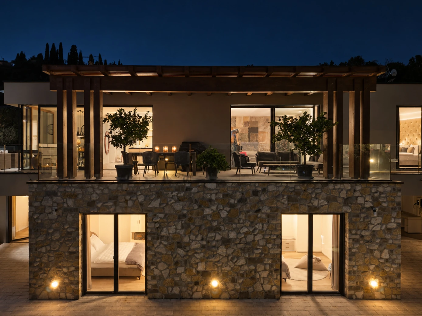 Villa facade at night, with illuminated rooms behind full-height windows and stone-clad walls. | Only on SopranoVillas