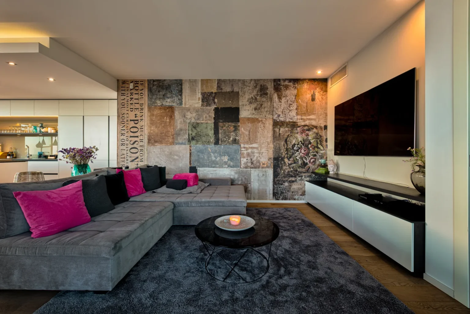 Living room with a grey corner sofa, pink cushions and a television against a textured feature wall. | Only on SopranoVillas