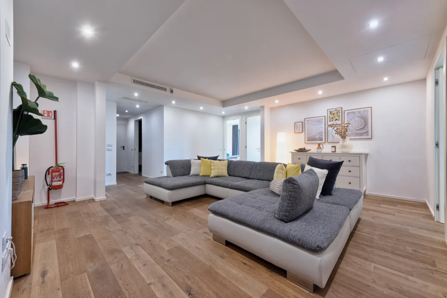 Living room with a grey sectional sofa, yellow cushions and framed artwork above a white sideboard. | Only on SopranoVillas