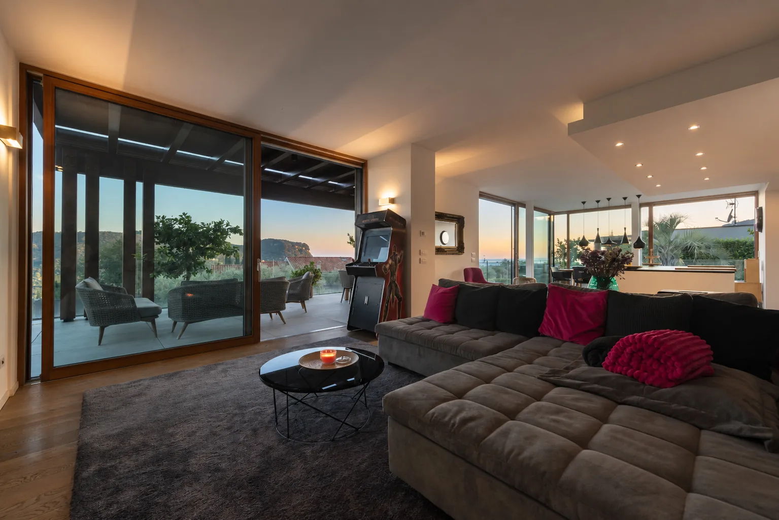 Living area with a grey sofa and glass doors beside the covered terrace, kitchen and dining space. | Only on SopranoVillas