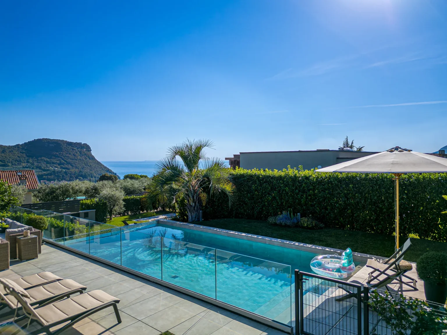Swimming pool with sun loungers, a glass railing and a view towards the lake. | Only on SopranoVillas