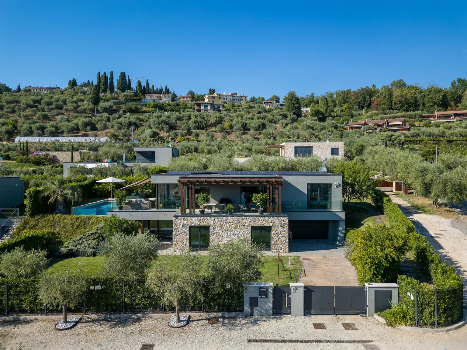 Front view of the modern villa with stone cladding, a garden and a pool on the upper terrace. | Only on SopranoVillas