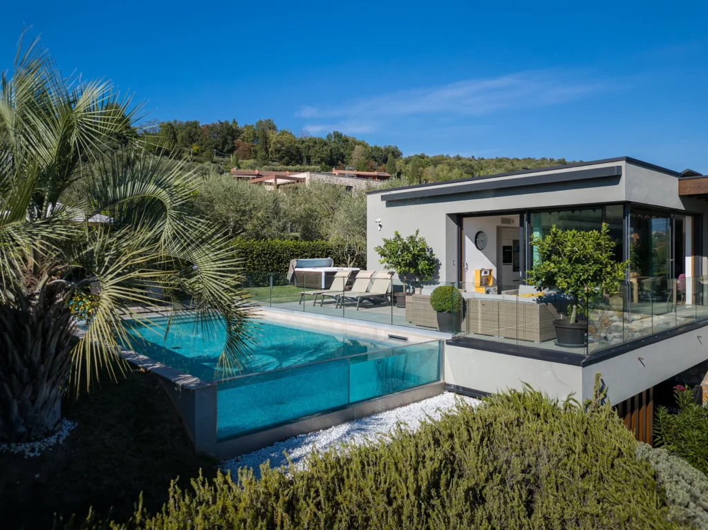 Swimming pool beside the villa's glass-fronted living area, with sun loungers and palm trees. | Only on SopranoVillas